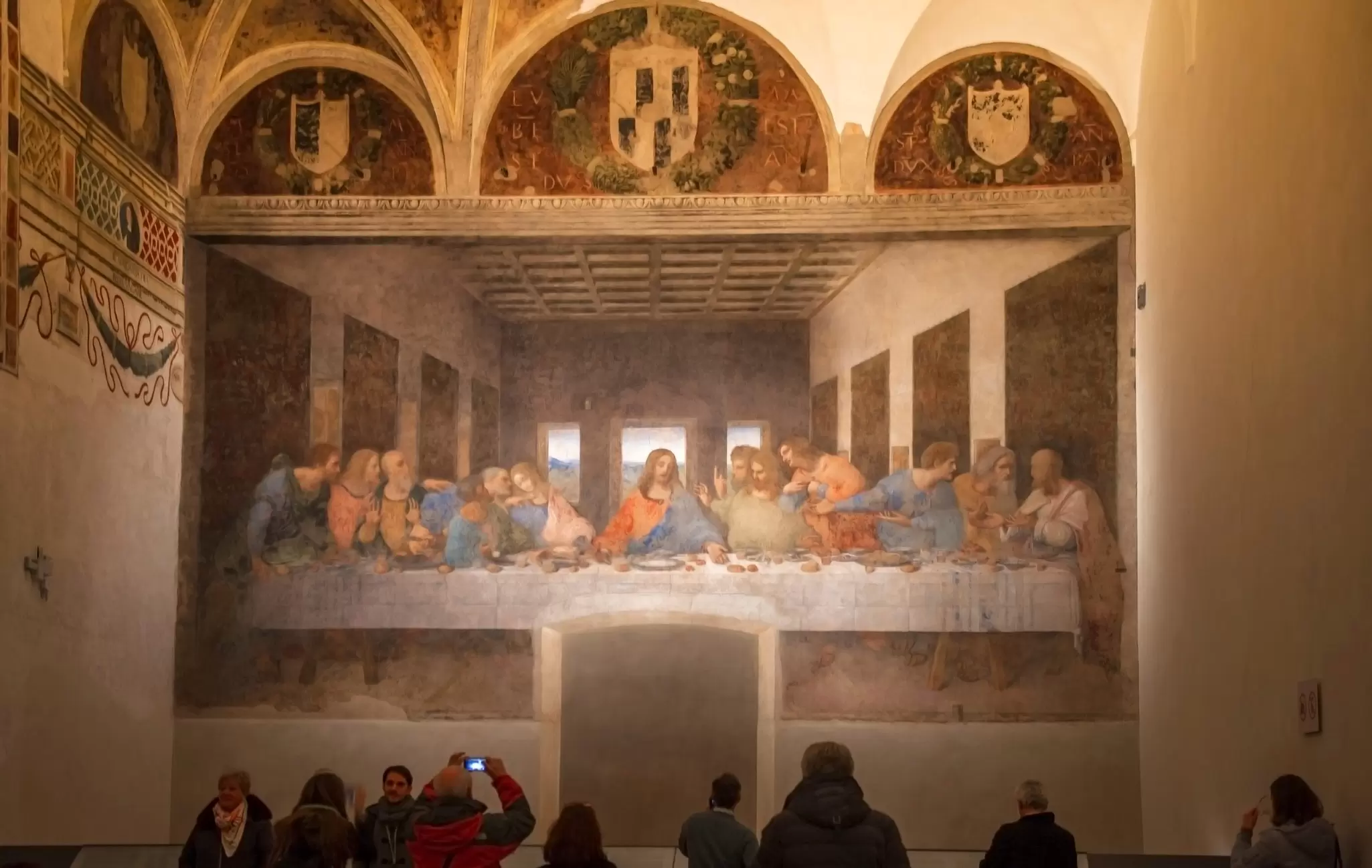 Tourists examining and taking pictures of The Last Supper masterpiece in the city church.