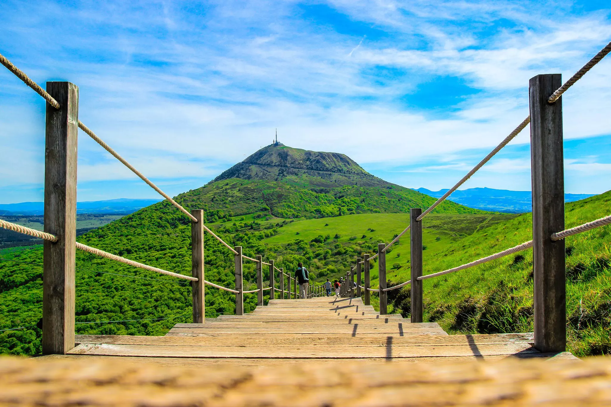 A wooden walkway with steps leading towards the dome of an extinct volcano, covered in greenery.
