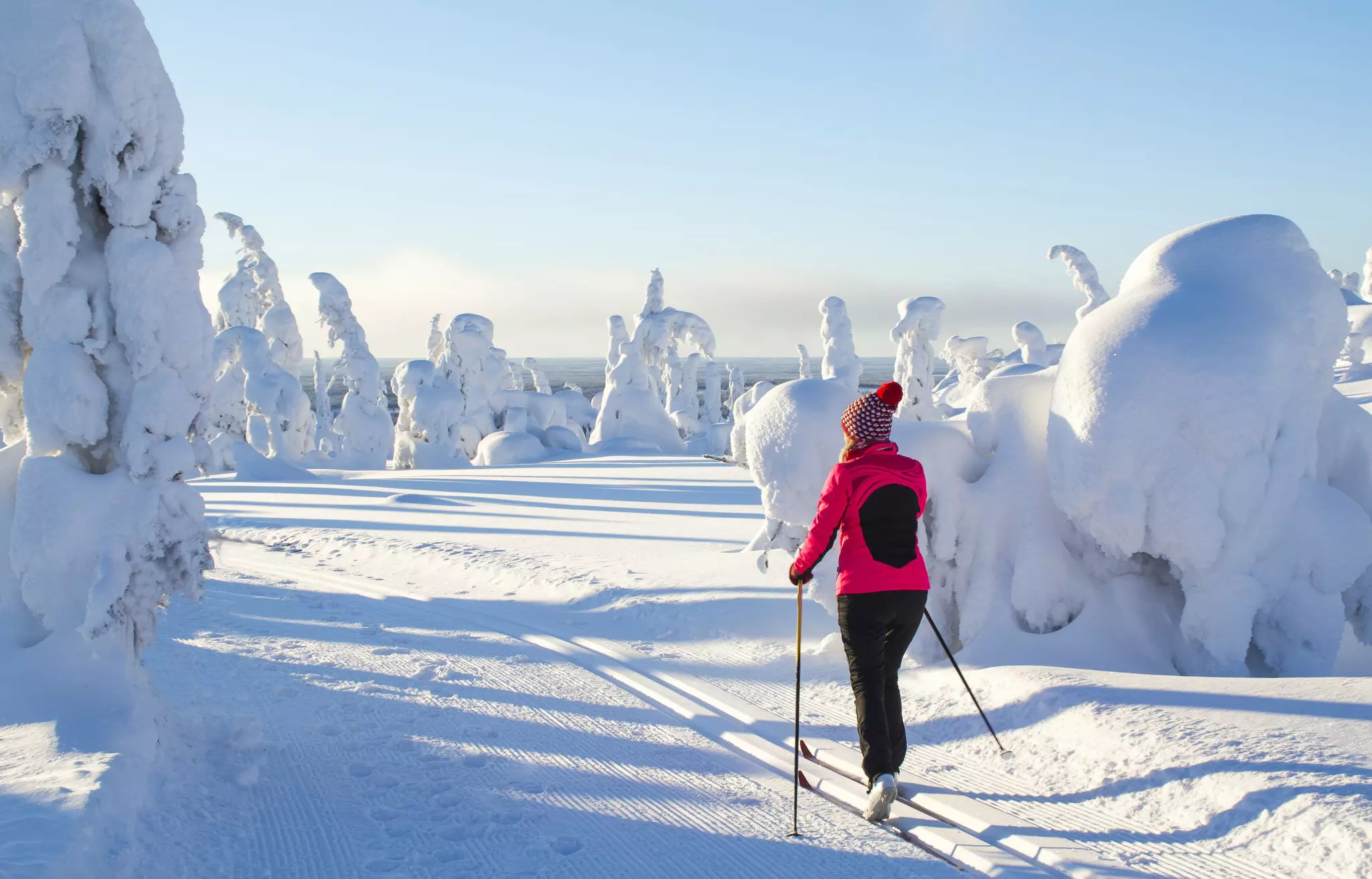 A skier in a pink jacket and black pants in a snow-covered landscape in Finland.