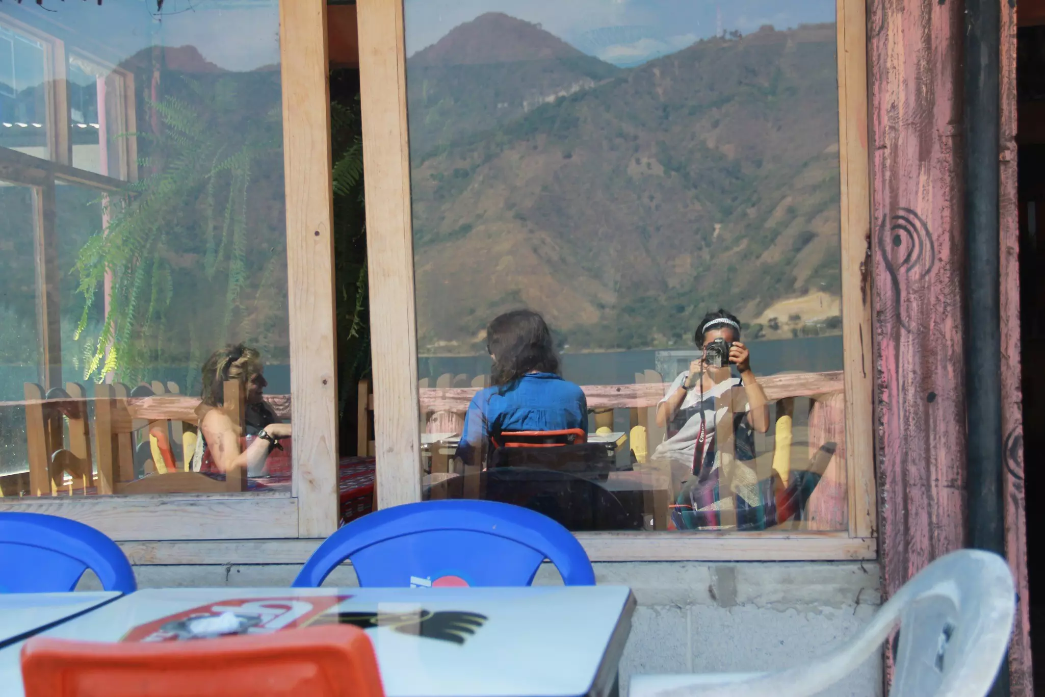 A woman takes a photograph of herself and friends reflected in a café window.