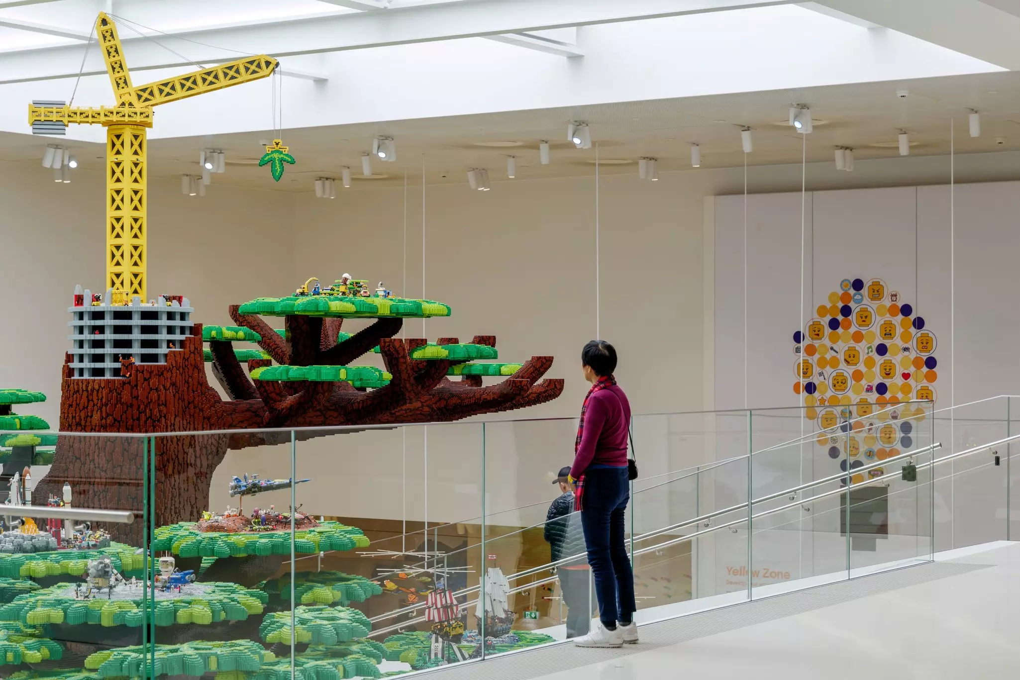 An adult and child look at a tree made from plastic bricks in the light-filled atrium of a museum.