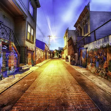 Painted figures and flowers cover both walls of a brick-paved lane at dusk.