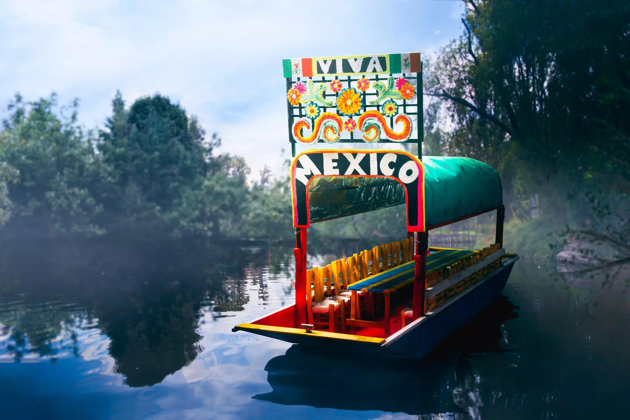 A scale model of a colorful canal boat with a sign reading "Viva Mexico" floating on a hazy canal.