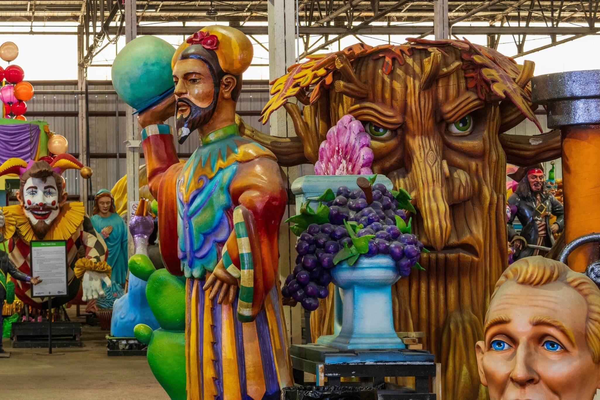 Giant fibreglass figures crowd a warehouse: a bearded king, a gnarled tree face with green eyes and an urn of grapes.