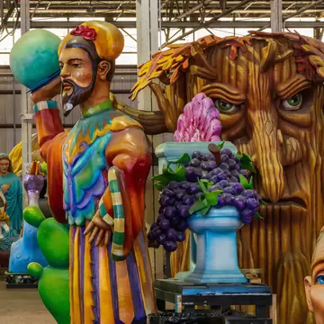 Giant fibreglass figures crowd a warehouse: a bearded king, a gnarled tree face with green eyes and an urn of grapes.