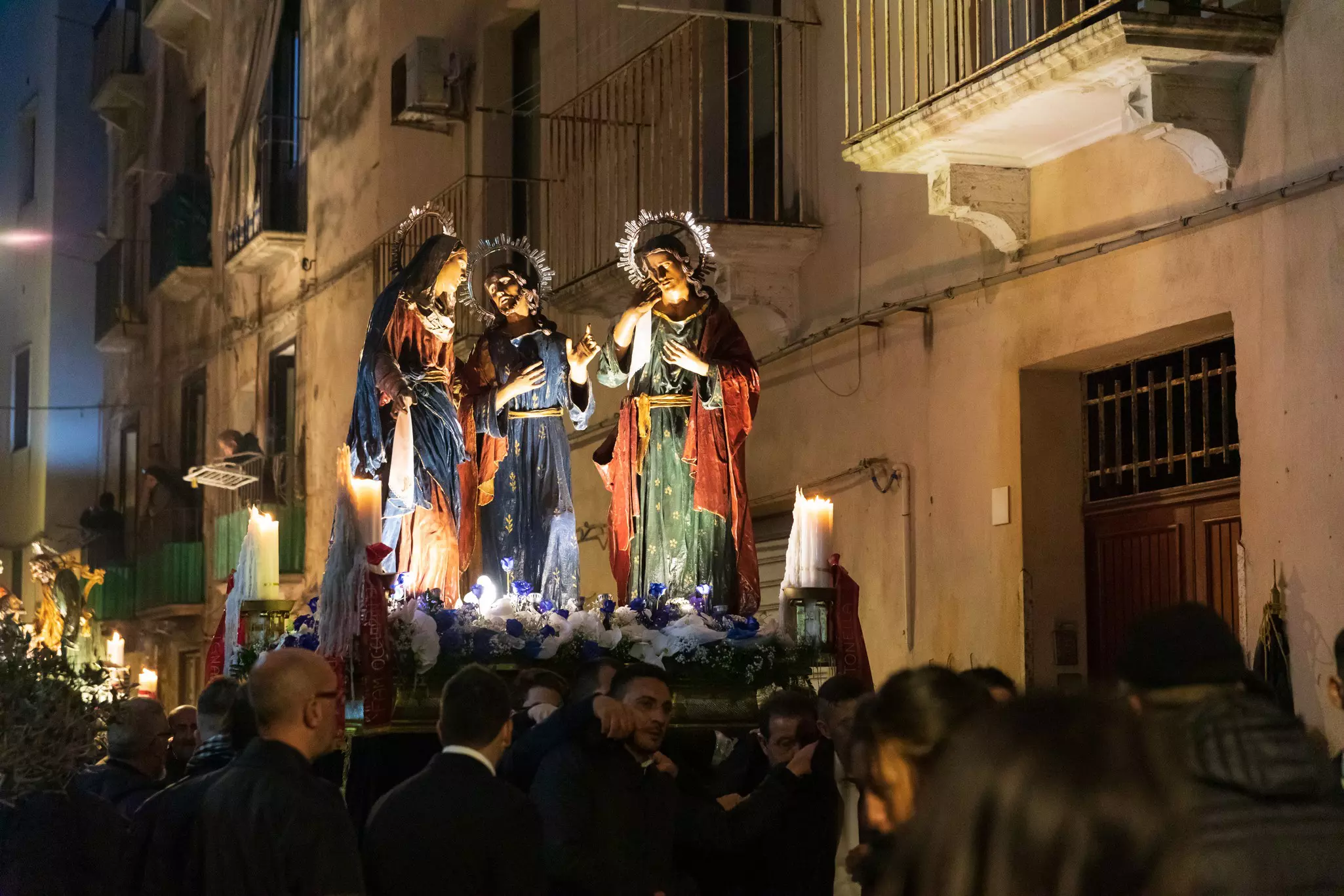 Figurines of biblical figures are carried during a nighttime procession in a city.
