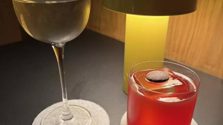 Close-up of two cocktails on a table with a lamp nearby.