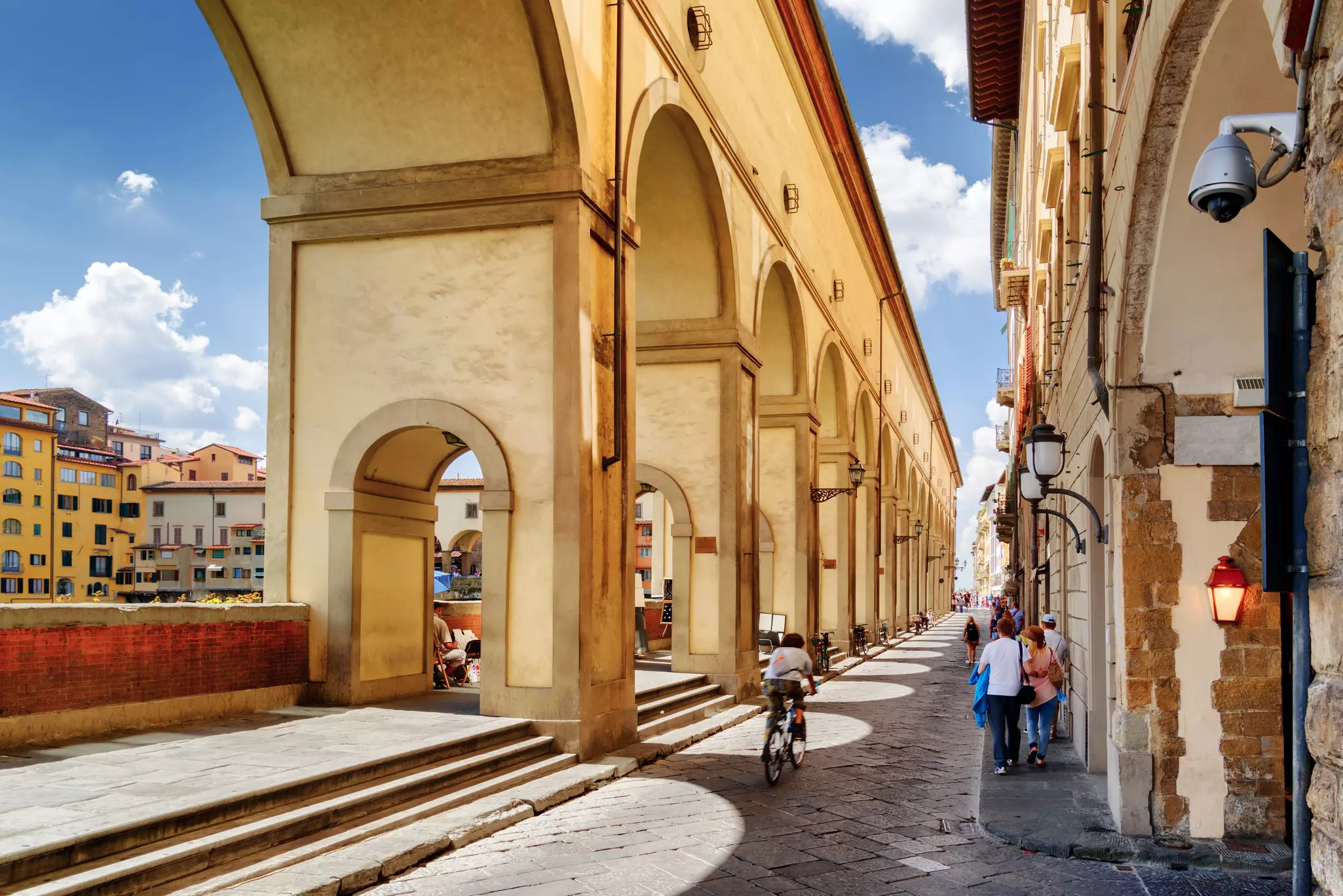 A cyclist and pedestrians near the arches of the Vasari Corridor (Corridoio Vasariano) on a sunny day