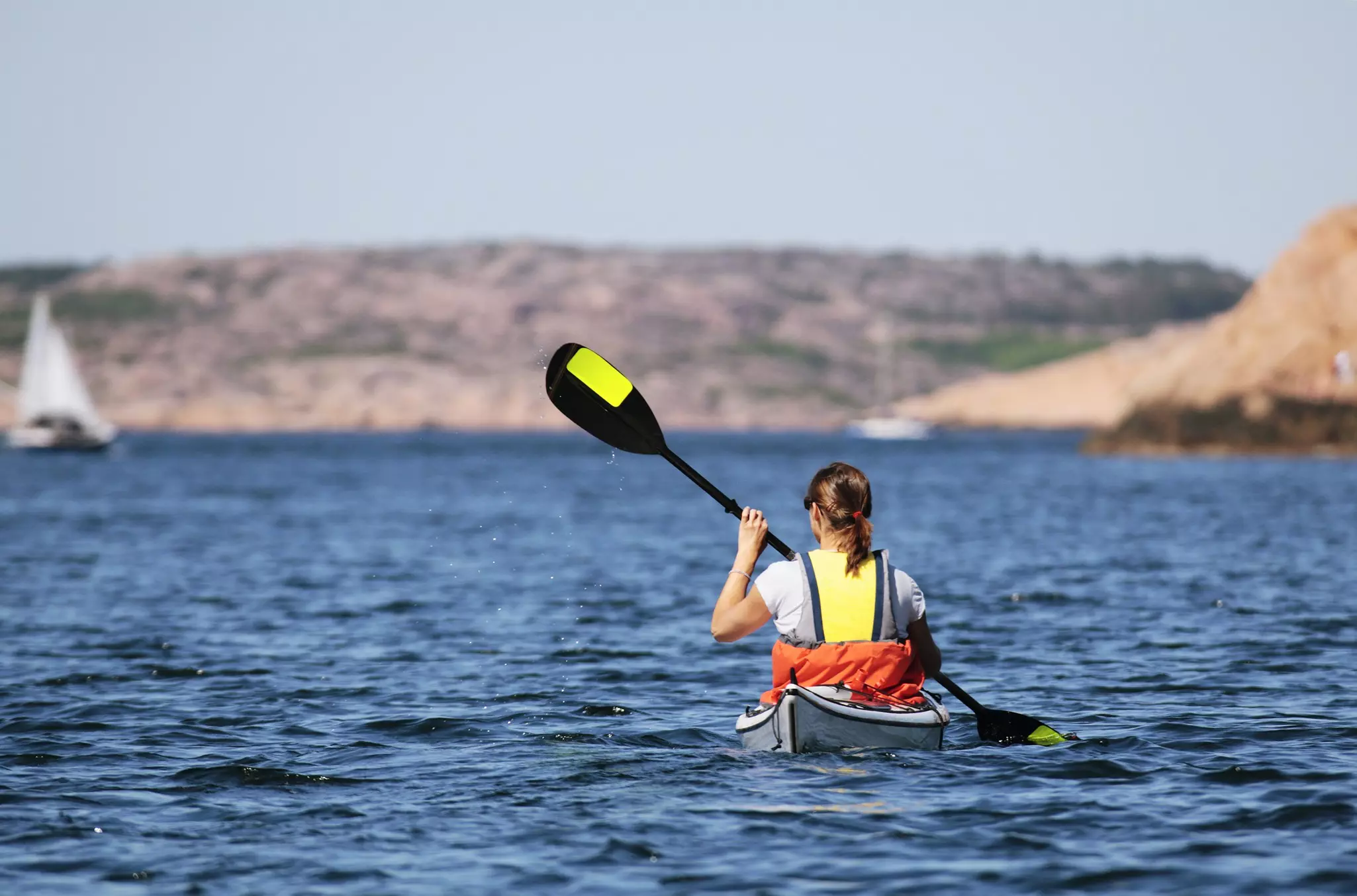 A woman raises her paddle in a kayak in the sea off the coast.