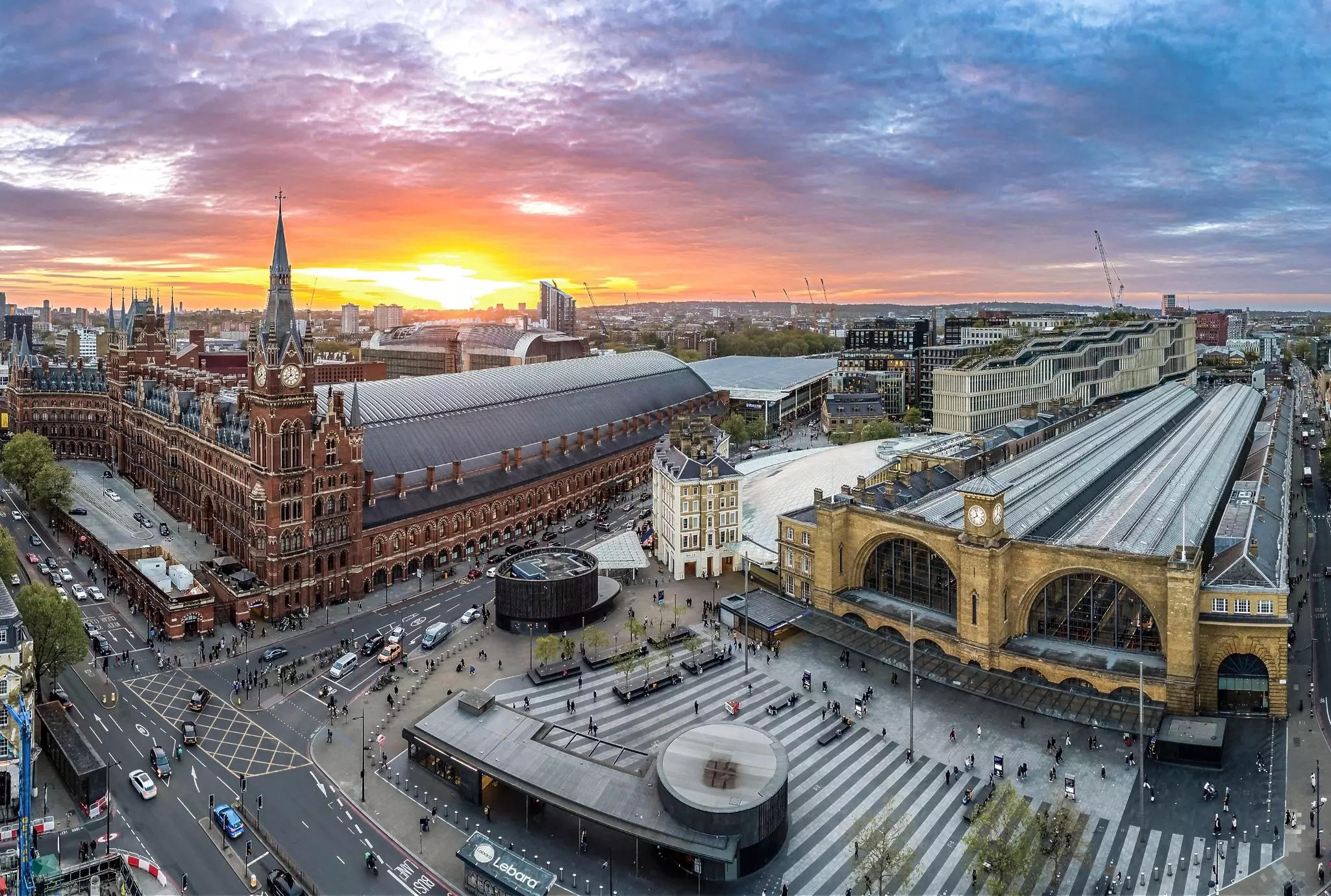 An aerial view of two train stations and an office headquarters in London, UK. Buildings are brick and the streets are busy with traffic.