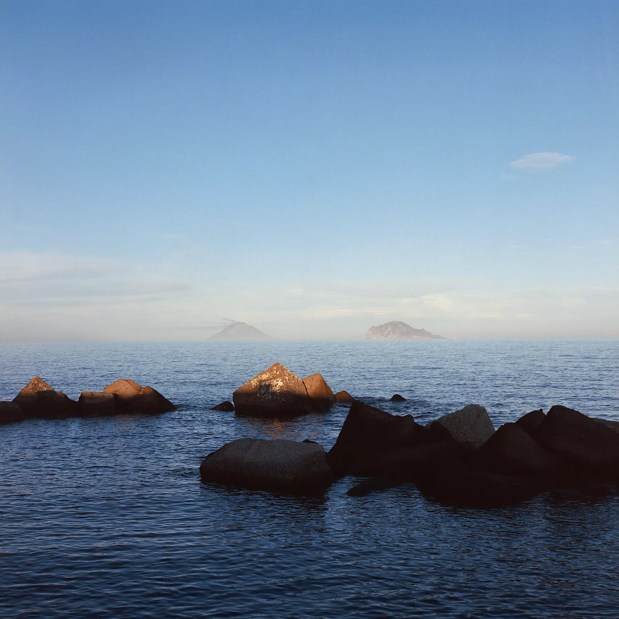 Shadows fall on rocks in the sea. Mist-covered islands are seen in the distance.