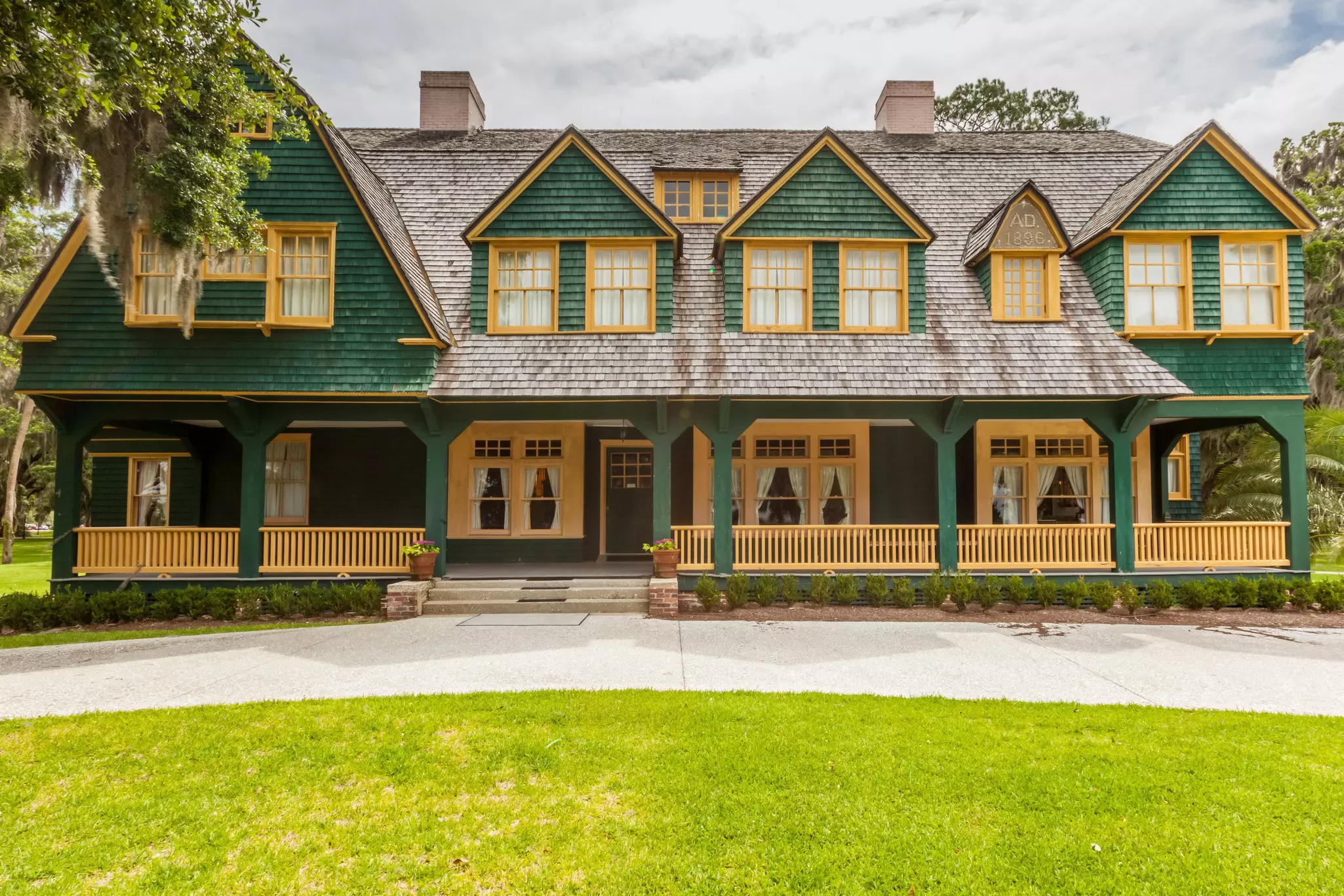 Green and yellow Cape Cod-style cottage shaded by a tree and surrounded by bright green grass on Jekyll Island