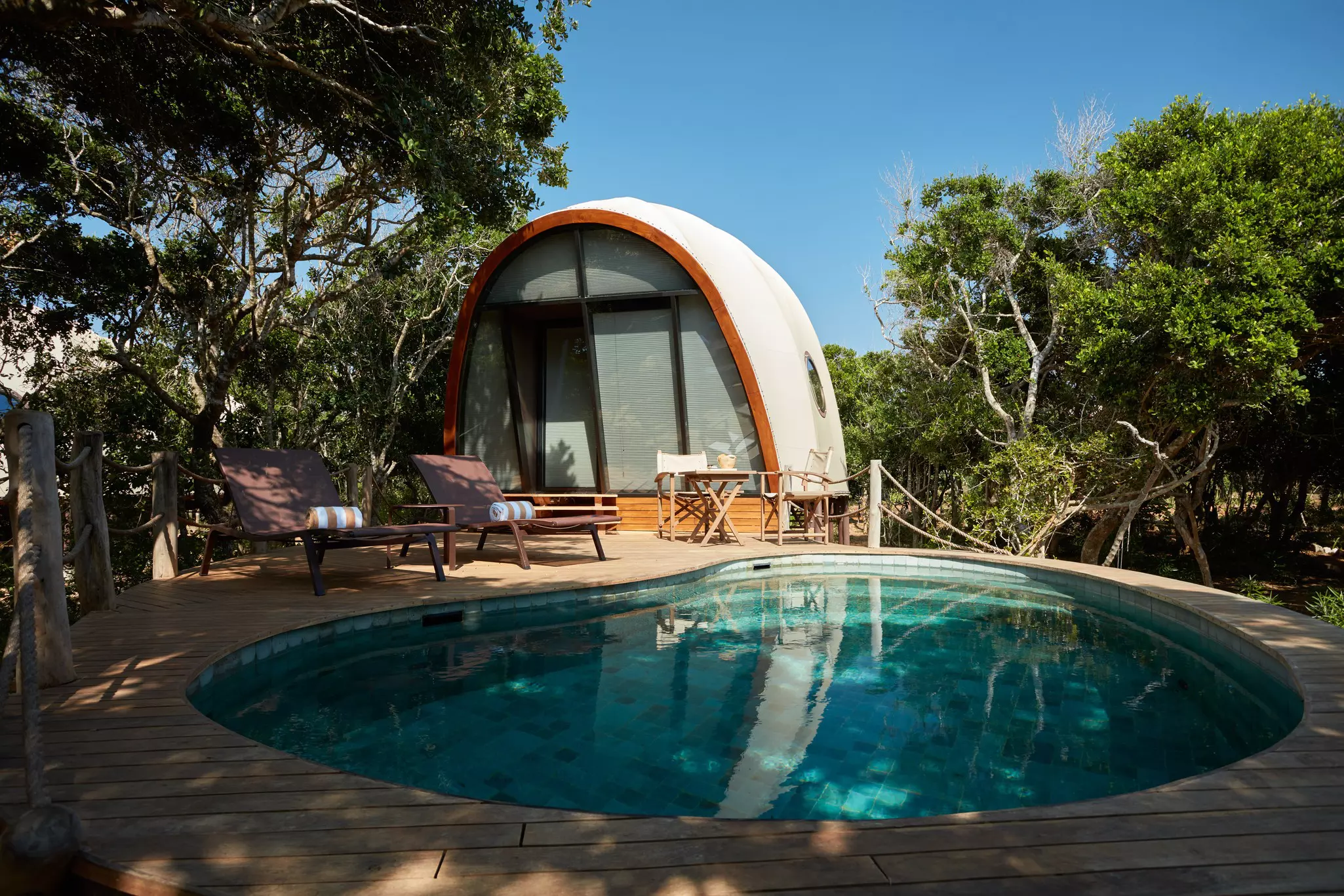 A cocoon-shaped tent with an individual plunge pool and two sunloungers secluded by trees.