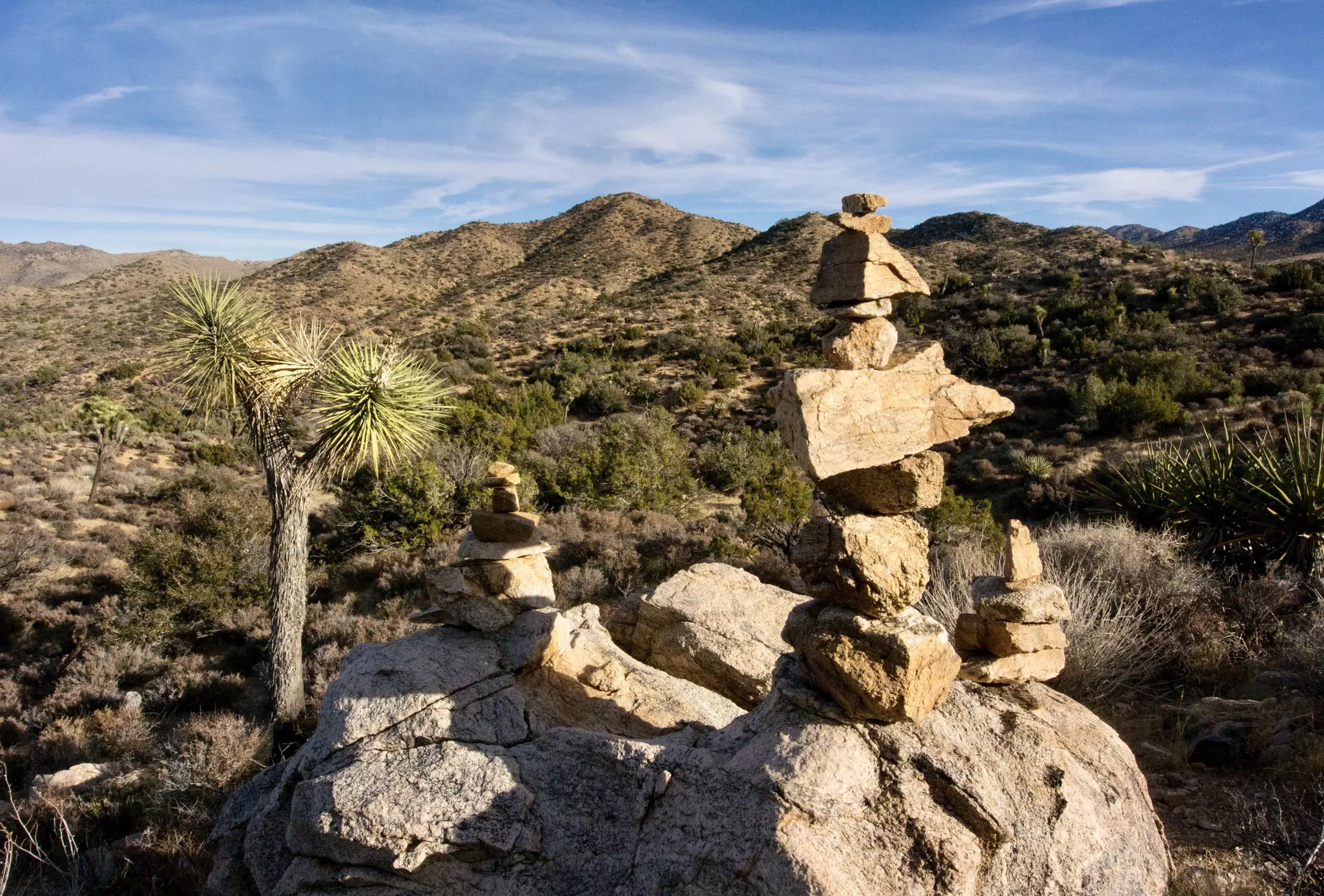 Hiker pass a stack of rocks marking a trail through a rocky, mountainous landscape.