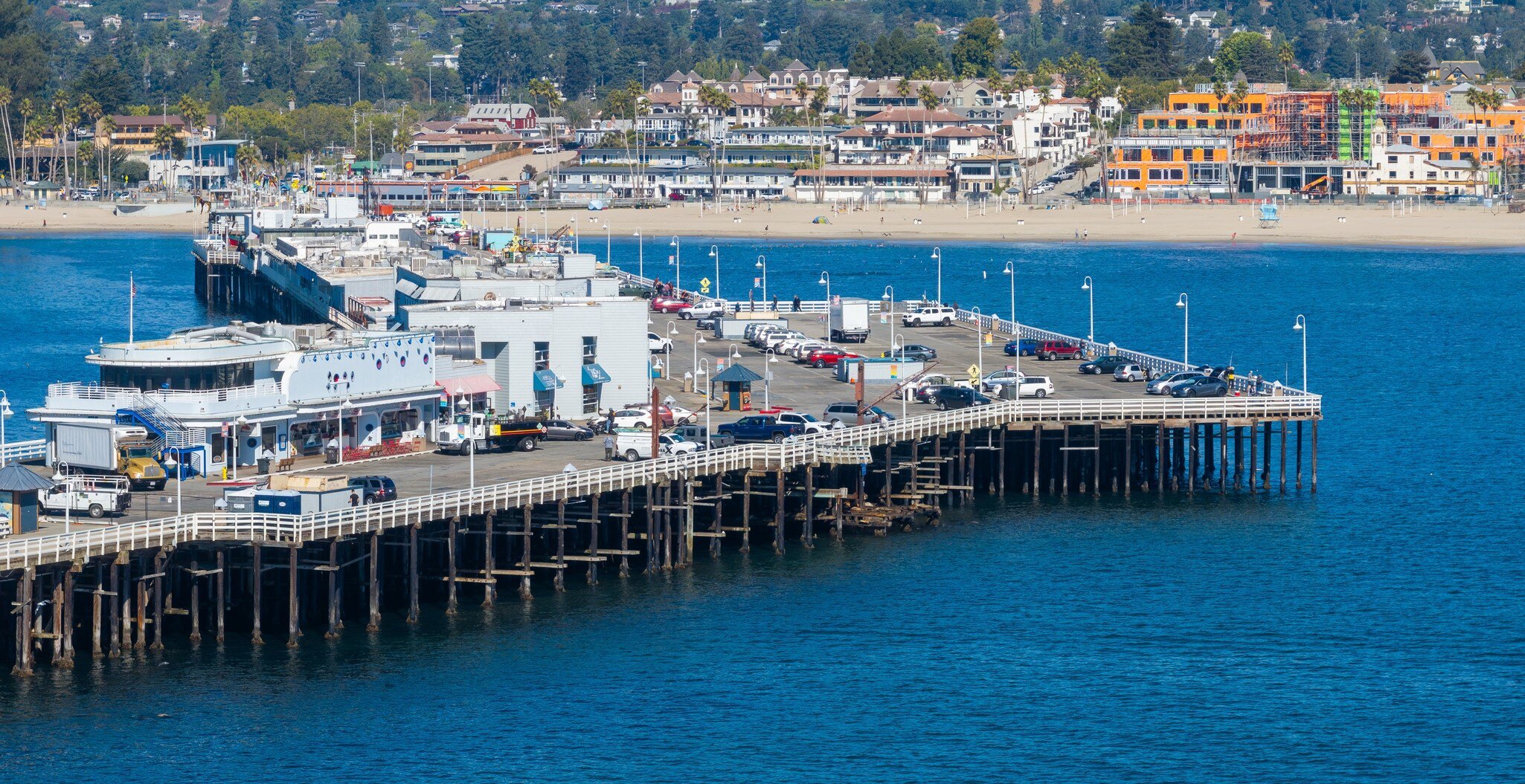 Santa Cruz Wharf extends into the Pacific Ocean, surrounded by parked cars and shops. The sandy beach and lush greenery complete the coastal scene., License Type: media, Download Time: 2026-08-09T22:56:48.000Z, User: LP_NZhan, Editorial: false, purchase_order: 65050 - Digital Destinations and Articles, job: App Content, client: Lonely Planet App, other: Nadine Zhan
