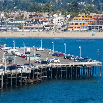 Santa Cruz Wharf extends into the Pacific Ocean, surrounded by parked cars and shops. The sandy beach and lush greenery complete the coastal scene., License Type: media, Download Time: 2026-08-09T22:56:48.000Z, User: LP_NZhan, Editorial: false, purchase_order: 65050 - Digital Destinations and Articles, job: App Content, client: Lonely Planet App, other: Nadine Zhan