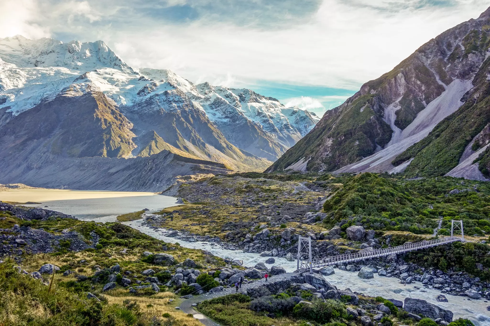 A metal bridge spanning a river surrounded by steep mountains