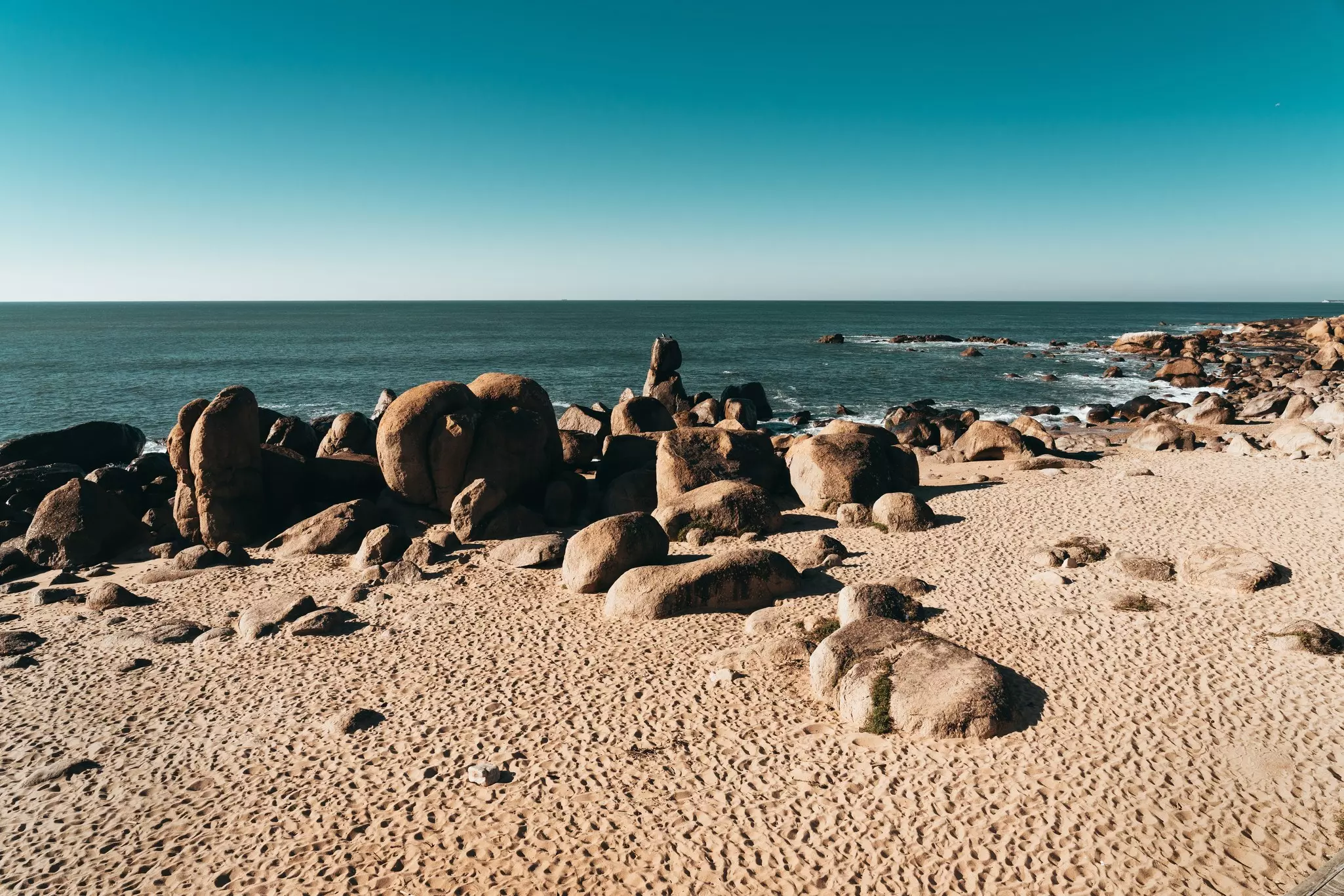 Boulders on sand with the ocean in the distance.