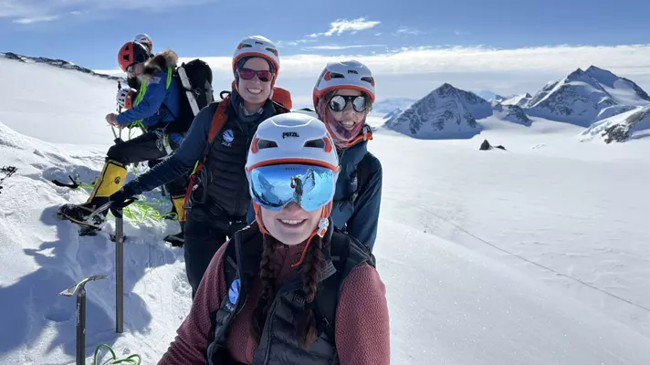 A group of people in cold-weather hiking gear pose together on a snow-covered mountain.