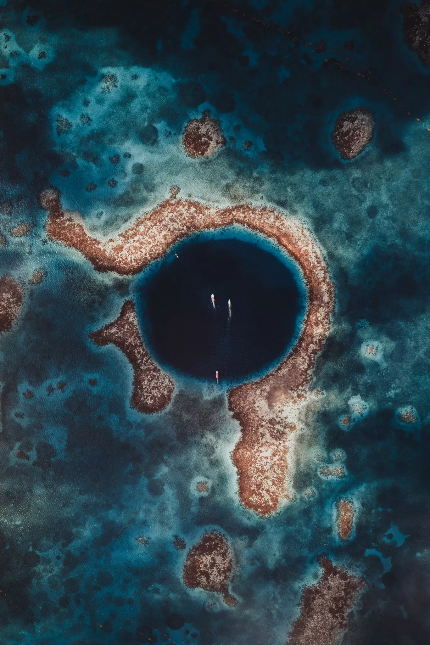 A vast blue circular crater out at sea with three dive boats moored within.
