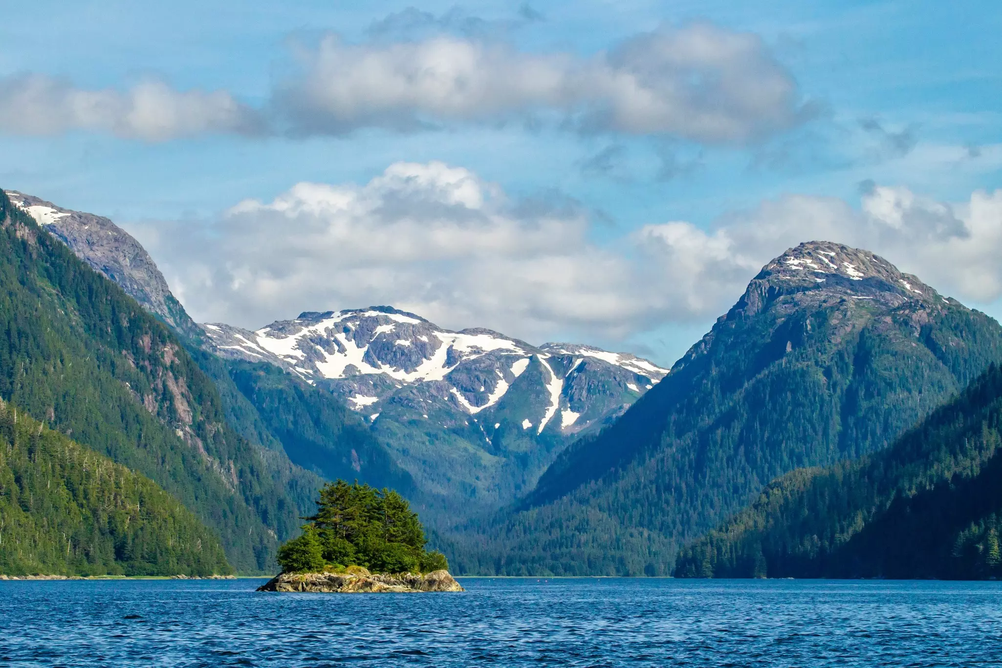 Forest-covered mountain slopes at the side of a waterway with a rocky islet