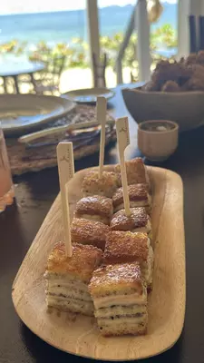 Small sandwich-like items arranged on an oblong wooden plate