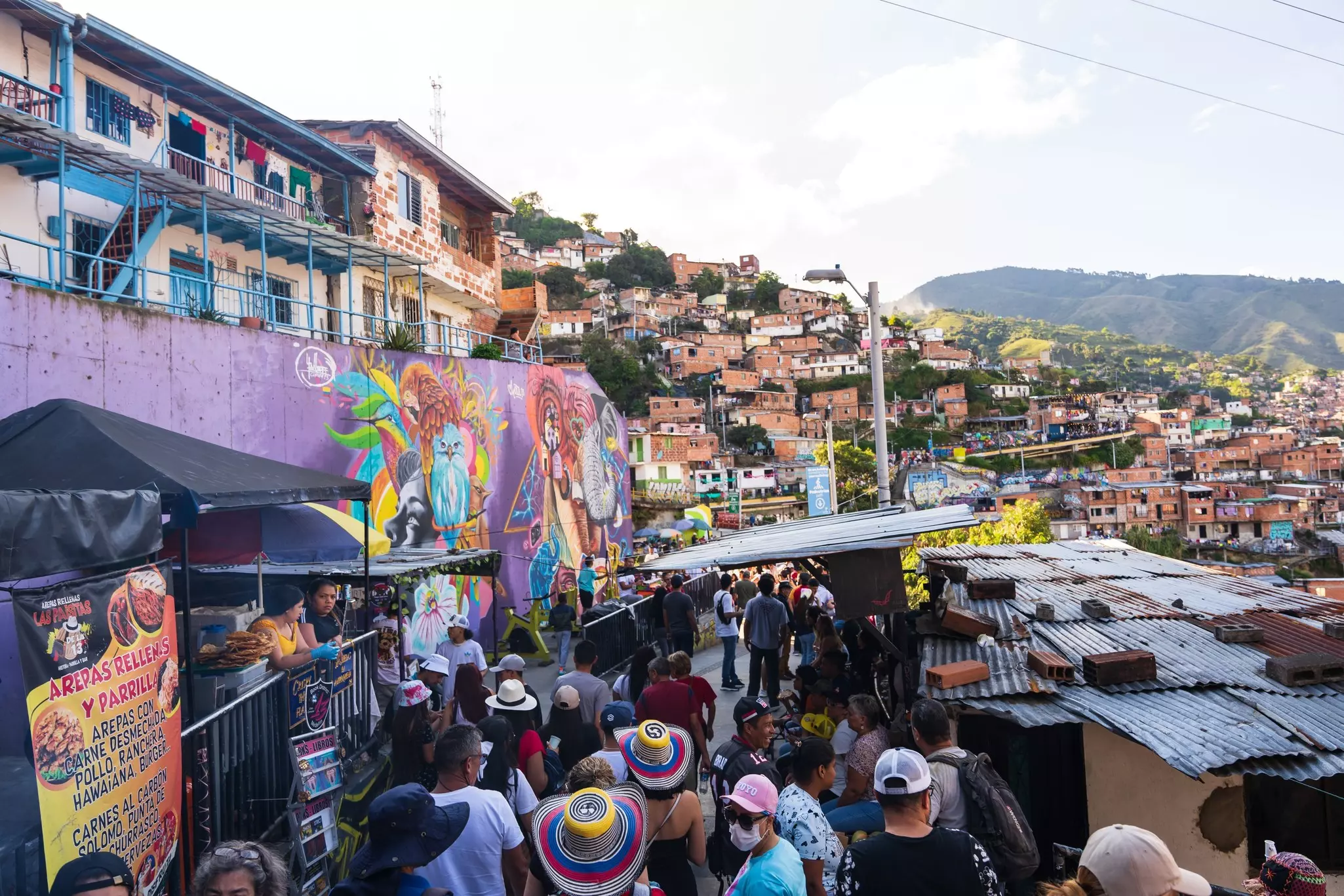 People crowd into a bar and food court with the buildings and hills of Medellín in the background.