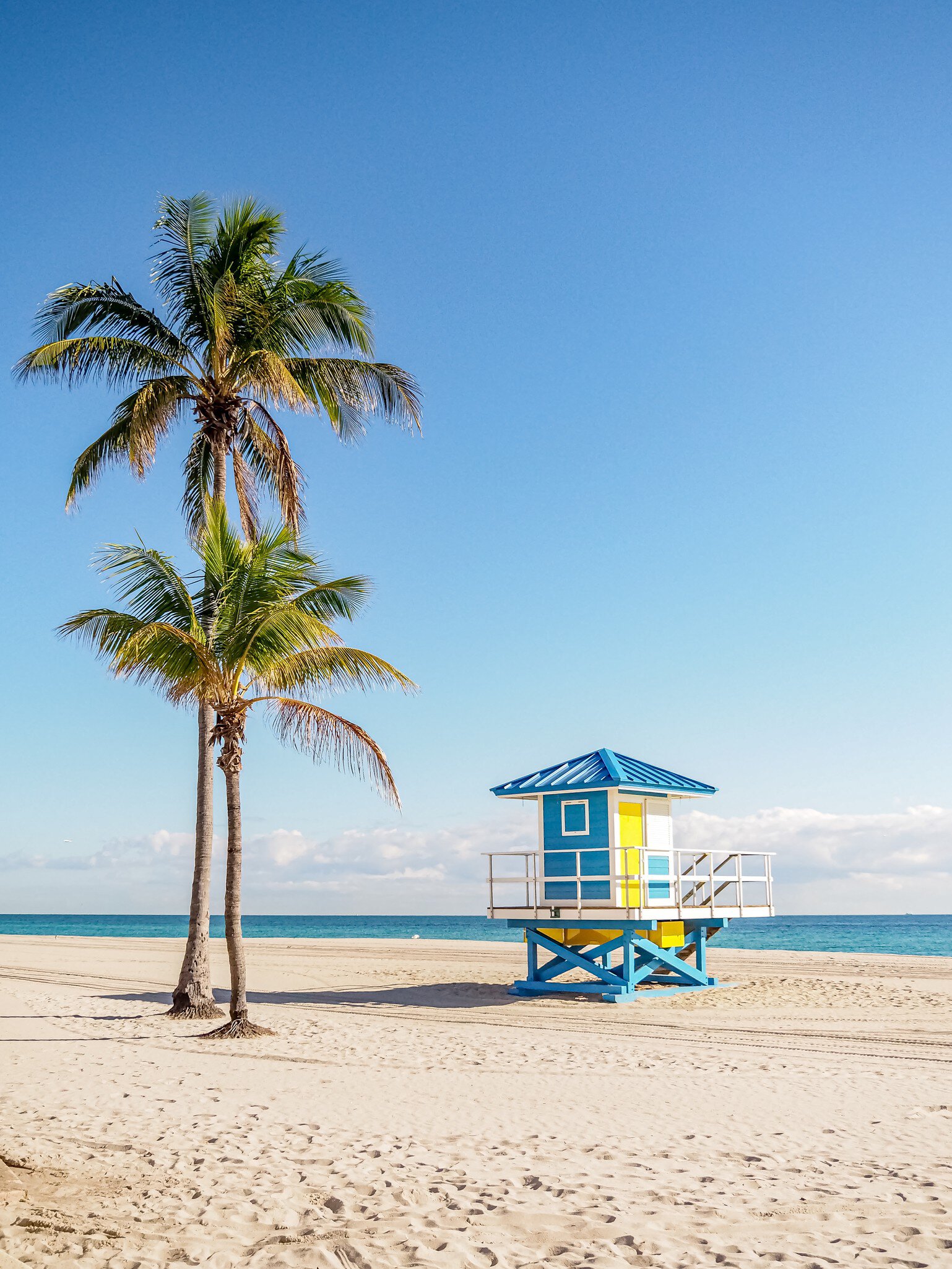 View of a colorful blue and yellow lifeguard station on the beach with palm trees on a sunny day in Miami, Florida.