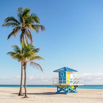 View of a colorful blue and yellow lifeguard station on the beach with palm trees on a sunny day in Miami, Florida.