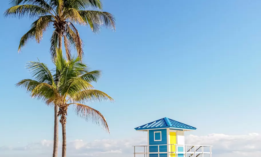 View of a colorful blue and yellow lifeguard station on the beach with palm trees on a sunny day in Miami, Florida.