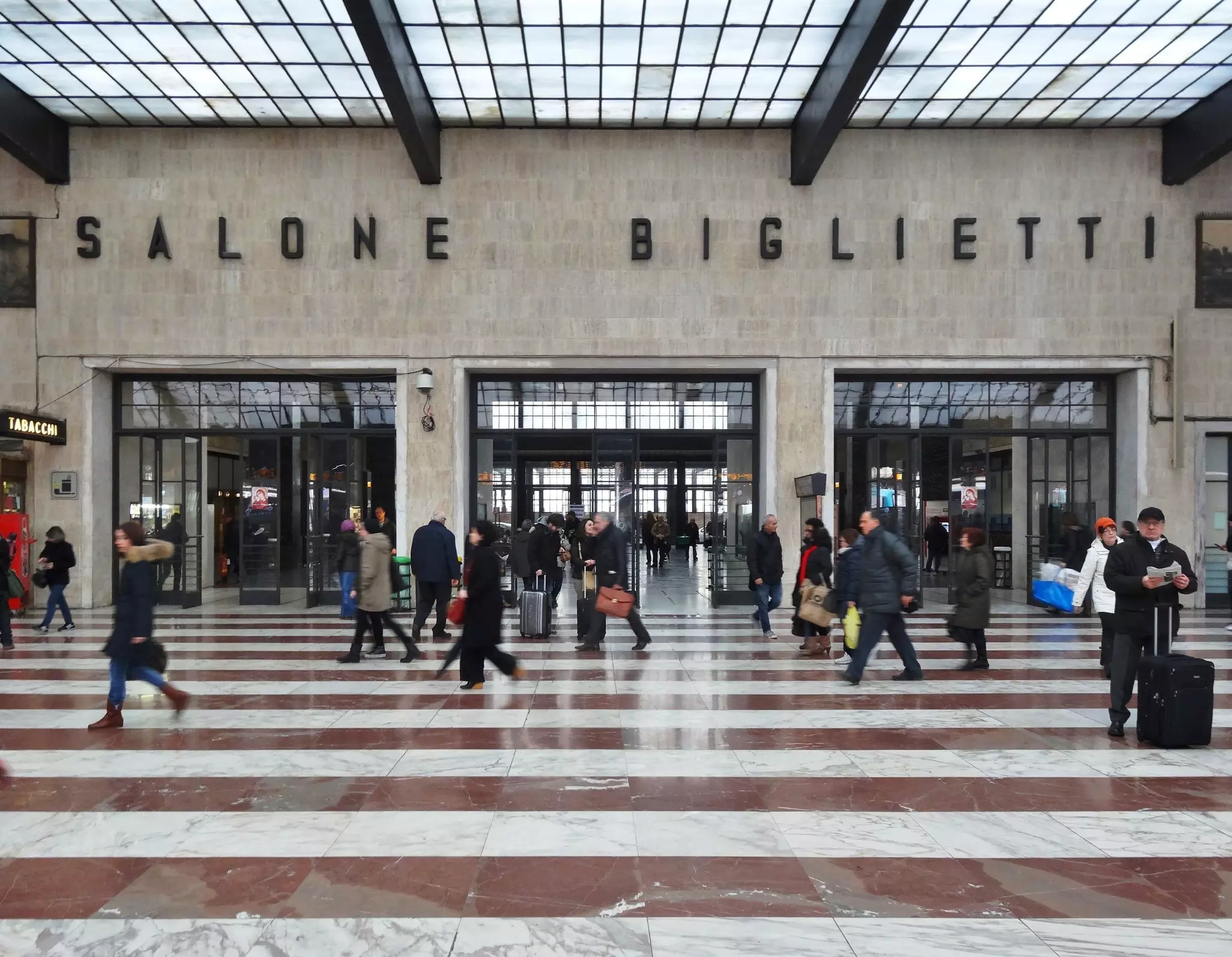 People walk past a busy train station ticket office