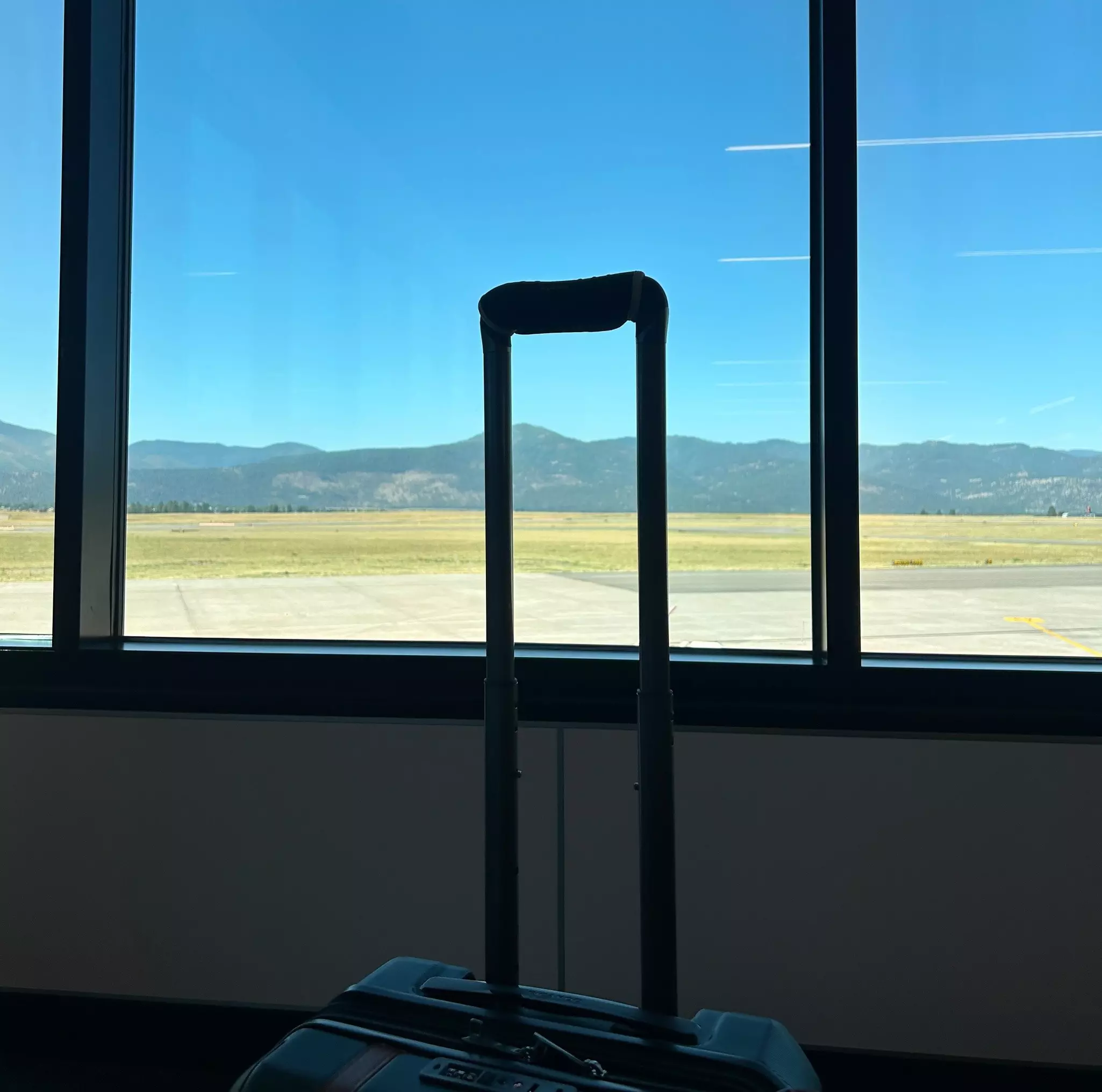 A suitcase in front of windows with an airport tarmac and mountains in the background