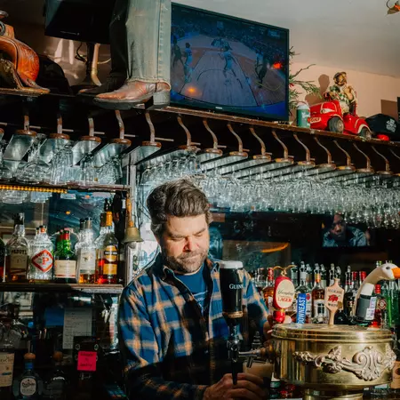A bartender pours a draft beer from a tap with glasses hanging from the ceiling behind him.