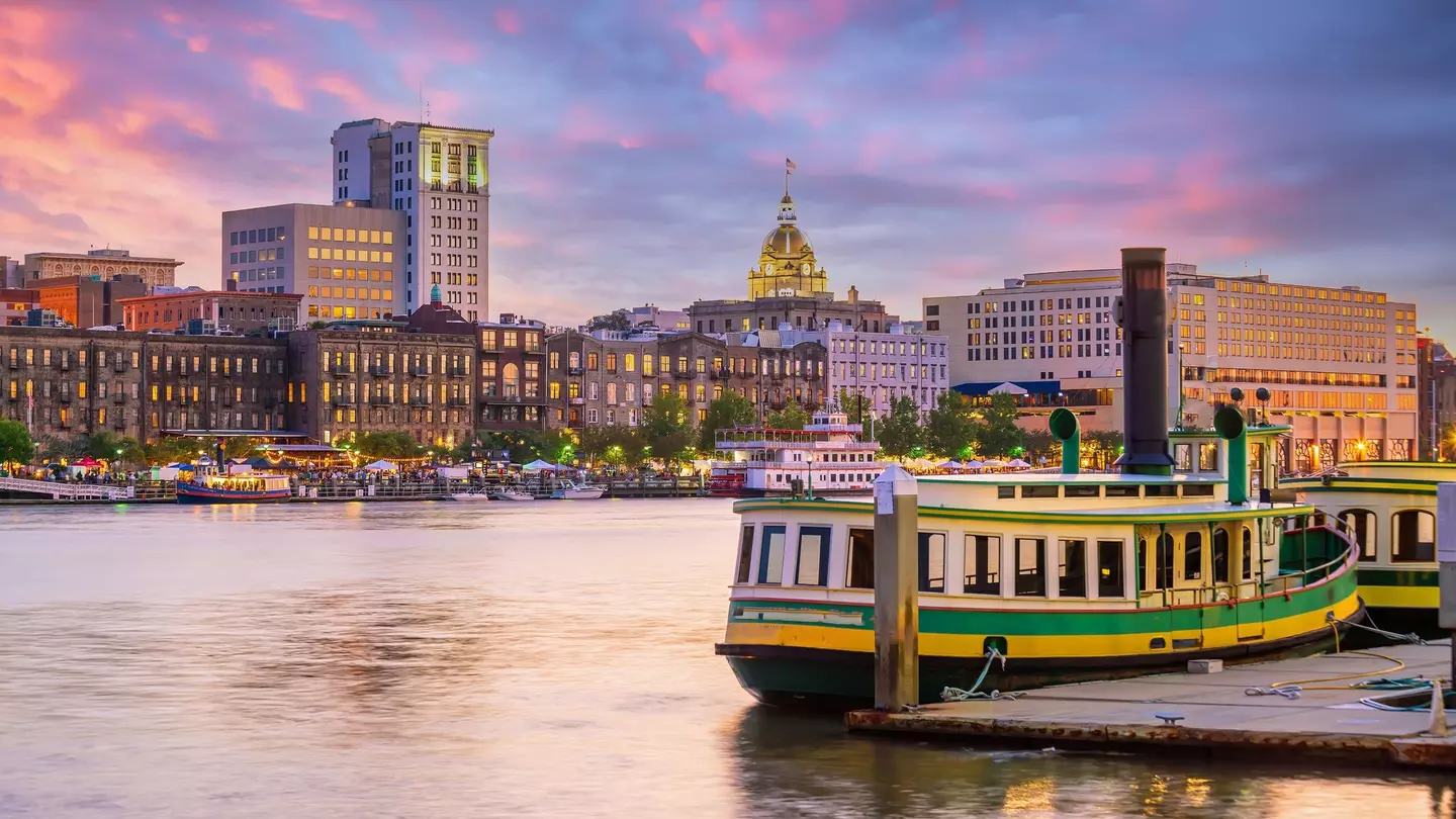 A green and white ferry is docked alongside a historic waterfront as the sun sets