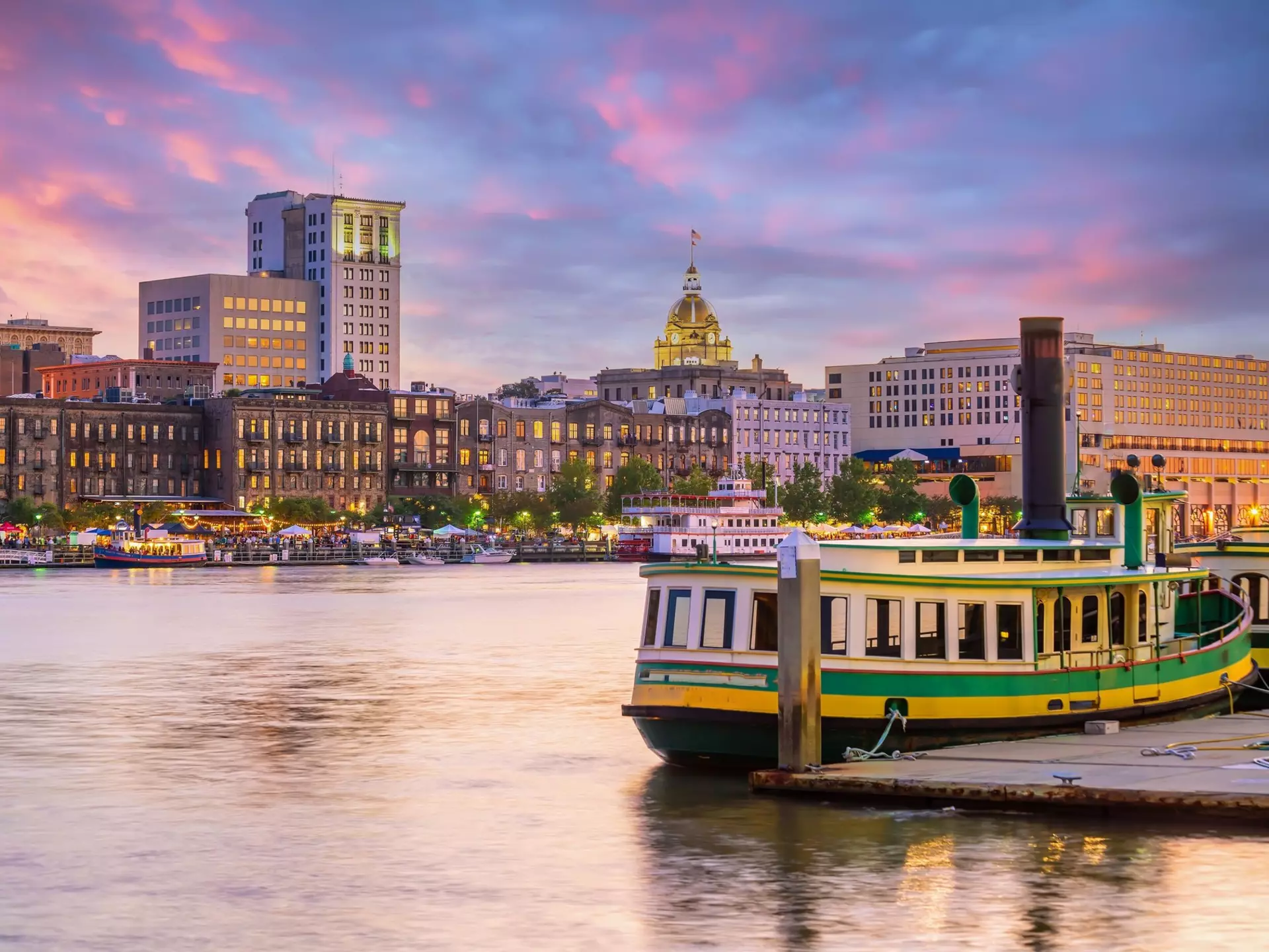 A green and white ferry is docked alongside a historic waterfront as the sun sets