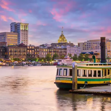 A green and white ferry is docked alongside a historic waterfront as the sun sets