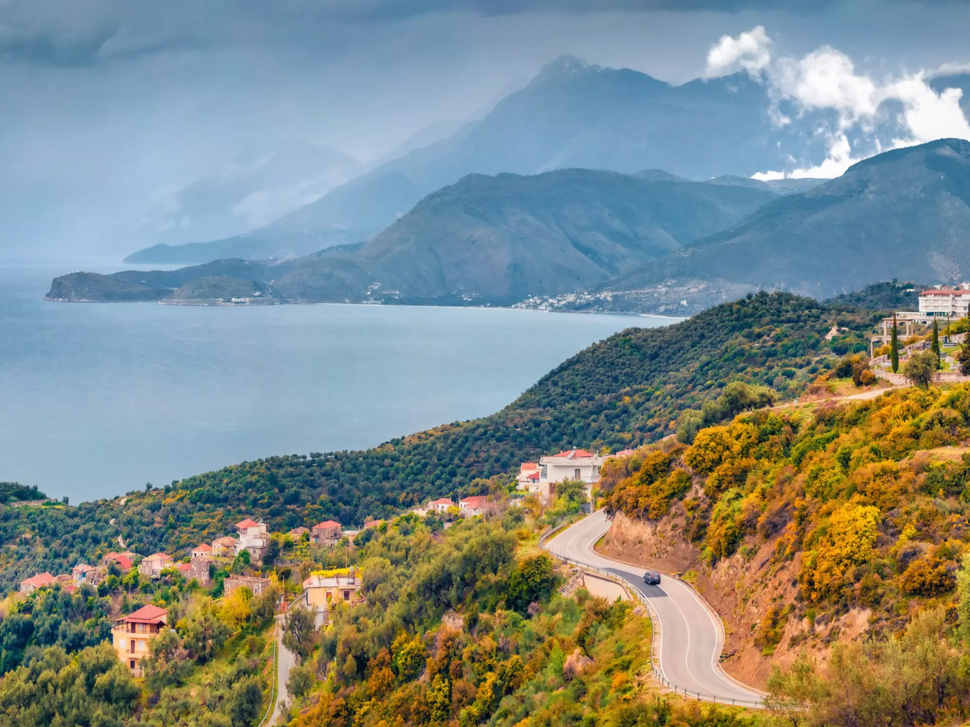 A typical Albanian landscape on the Adriatic shore with asphalt road and misty mountains leading toward the sea.