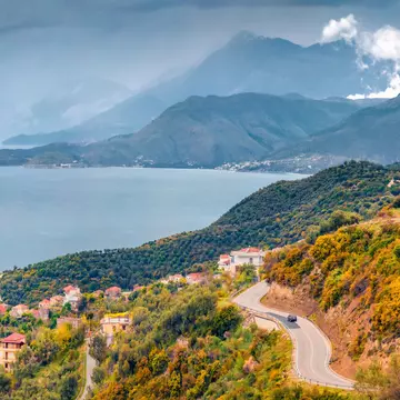 A typical Albanian landscape on the Adriatic shore with asphalt road and misty mountains leading toward the sea.