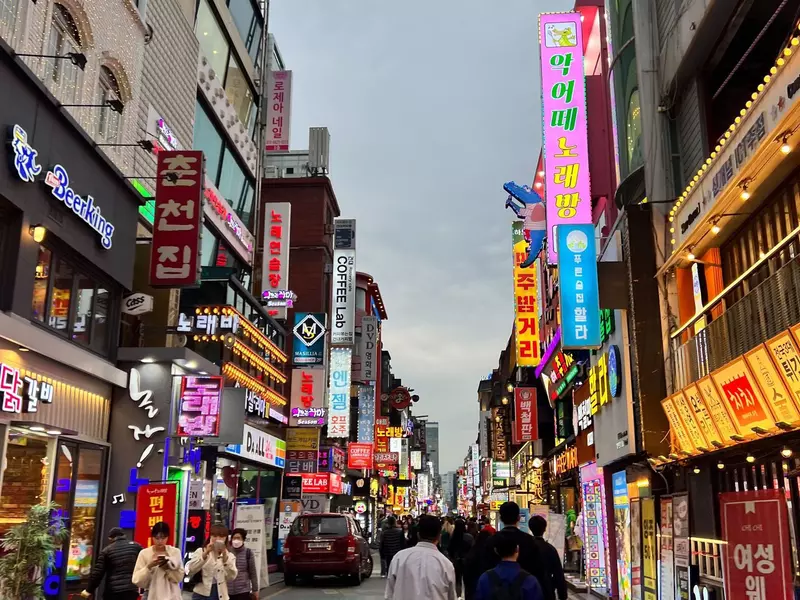 A street lined with huge neon signs lit up as evening comes