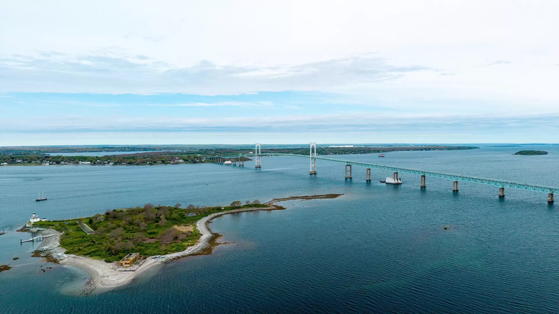 Rose Island and Newport Bridge aerial view, showing the historic lighthouse and military fort with the Claiborne Pell Bridge crossing Narragansett Bay in Newport, Rhode Island.