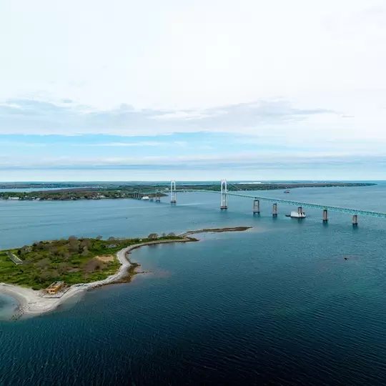 Rose Island and Newport Bridge aerial view, showing the historic lighthouse and military fort with the Claiborne Pell Bridge crossing Narragansett Bay in Newport, Rhode Island.