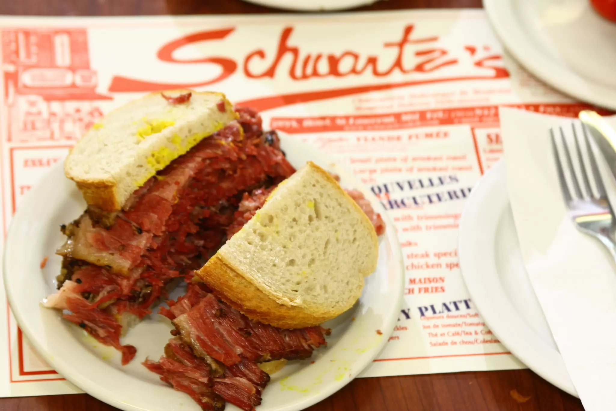 A sandwich filled with smoked meat is pictured on a paper placemat on a table at Schwartz’s Deli, Montréal