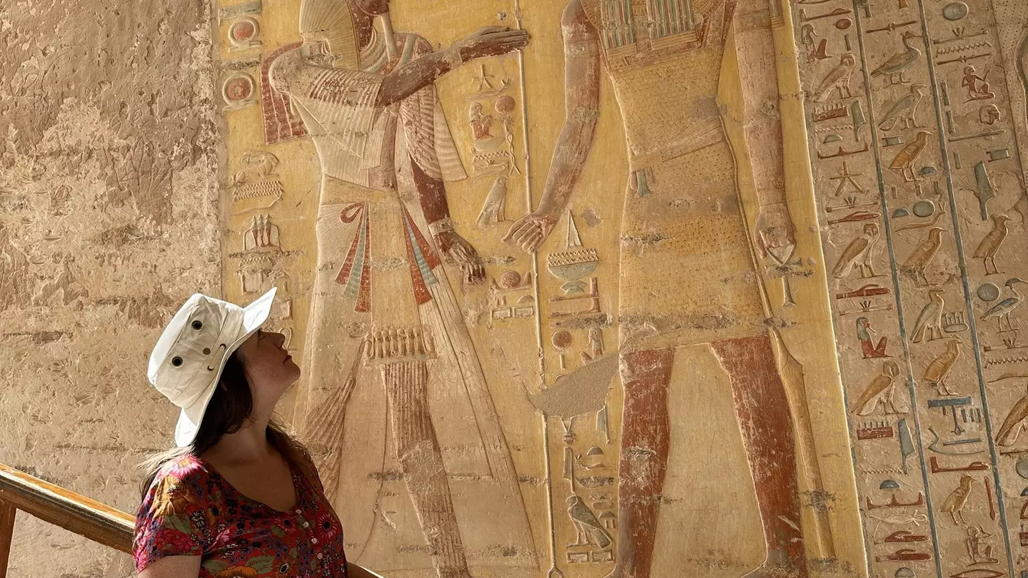 Woman in a red dress and a white hat looks at ancient Egyptian art