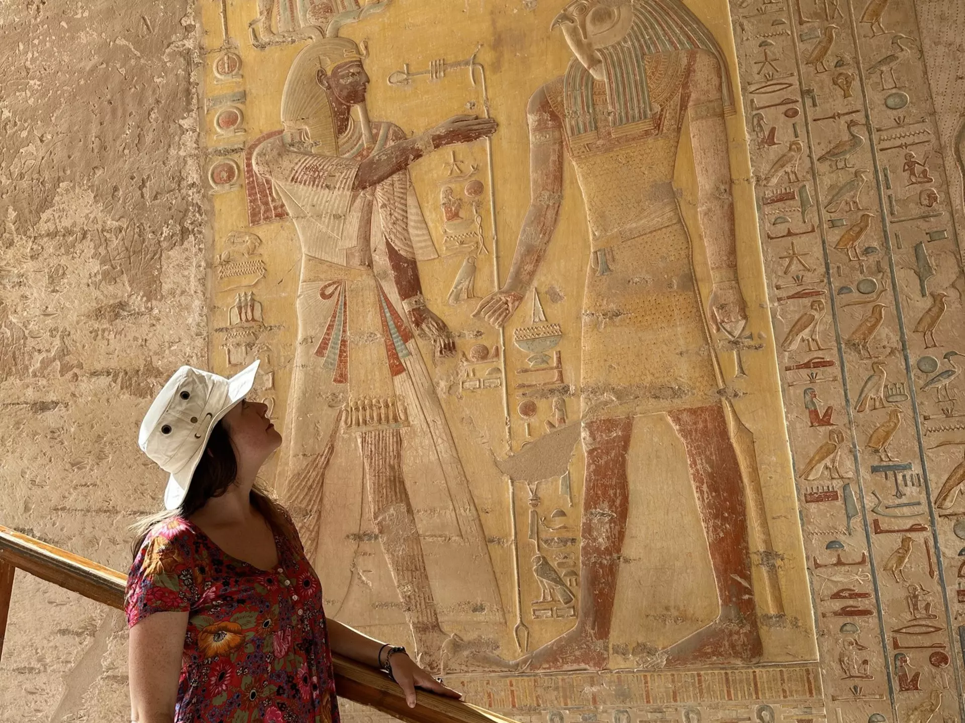 Woman in a red dress and a white hat looks at ancient Egyptian art