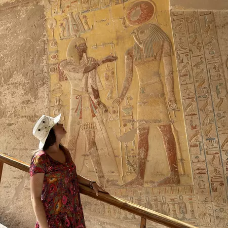 Woman in a red dress and a white hat looks at ancient Egyptian art