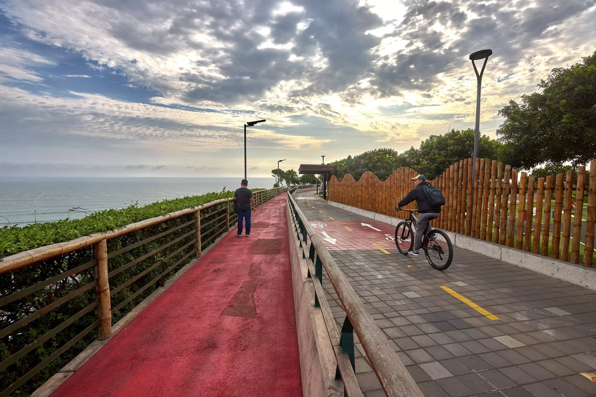 A cyclist rides along a bike path by waterfront cliffs in a city at dusk.