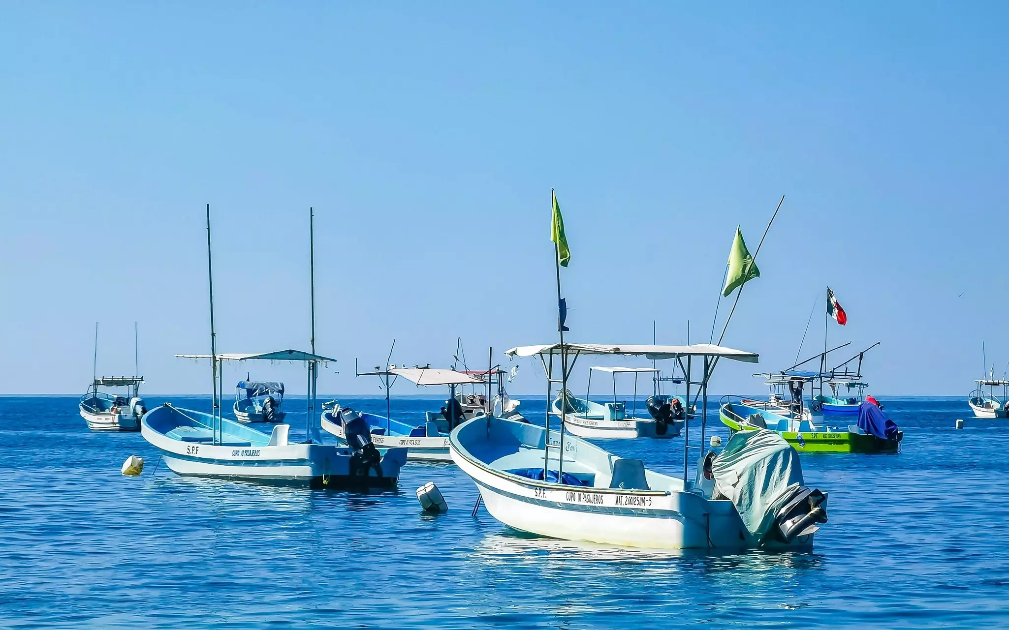 Small fishing boats, emtpy of people, moored in the ocean on a sunny day.