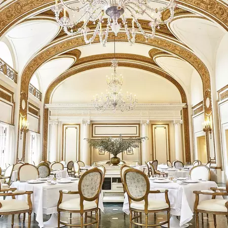 Ornate dining room with curved ceilings and upscale white and gold walls, tables, and chairs.