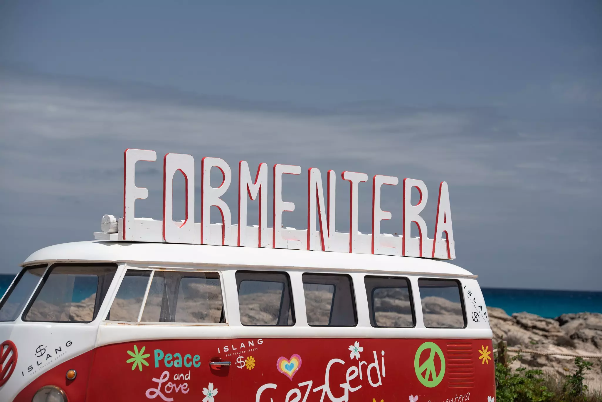 A VW campervan on a beach with a large sign on top that reads "Formentera"