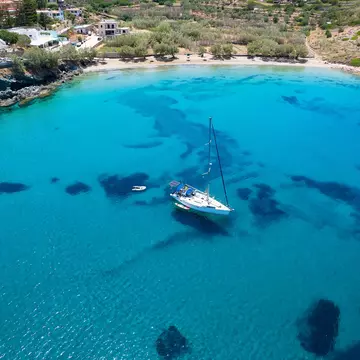 Aerial view of the beautiful Lotos Beach next to Kini bay at Syros island, Greece, with a sailboat moored over turquoise sea